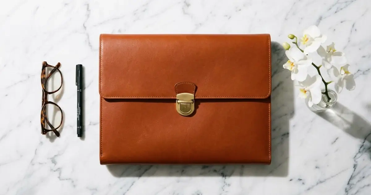 A closed leather folder with a brass latch on marble representing firm naming boundaries